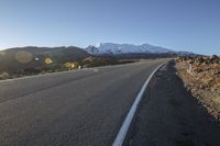 a long stretch of empty road with snow covered mountains behind it in the distance on a sunny day