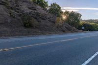 an empty road with a few signs and trees near by on a hillside, at sunset