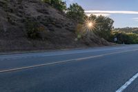 an empty road with a few signs and trees near by on a hillside, at sunset