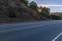 an empty road with a few signs and trees near by on a hillside, at sunset