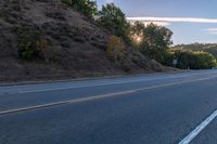 an empty road with a few signs and trees near by on a hillside, at sunset