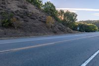 an empty road with a few signs and trees near by on a hillside, at sunset