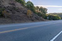 an empty road with a few signs and trees near by on a hillside, at sunset