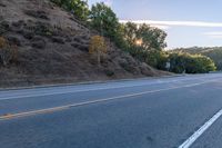 an empty road with a few signs and trees near by on a hillside, at sunset