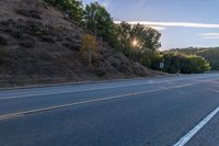 an empty road with a few signs and trees near by on a hillside, at sunset