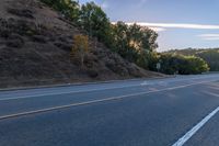 an empty road with a few signs and trees near by on a hillside, at sunset