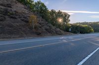 an empty road with a few signs and trees near by on a hillside, at sunset