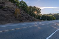 an empty road with a few signs and trees near by on a hillside, at sunset