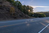 an empty road with a few signs and trees near by on a hillside, at sunset