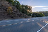 an empty road with a few signs and trees near by on a hillside, at sunset