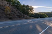 an empty road with a few signs and trees near by on a hillside, at sunset