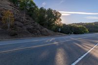 an empty road with a few signs and trees near by on a hillside, at sunset