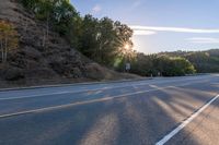 an empty road with a few signs and trees near by on a hillside, at sunset