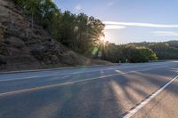 an empty road with a few signs and trees near by on a hillside, at sunset