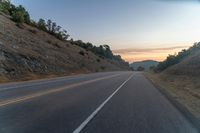 the road is empty while the sun sets behind a hill on a cloudy day in an area with no clouds