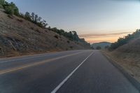 the road is empty while the sun sets behind a hill on a cloudy day in an area with no clouds