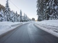 there is a long empty road surrounded by trees in the winter with snow on it
