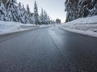 there is a long empty road surrounded by trees in the winter with snow on it