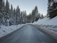 there is a long empty road surrounded by trees in the winter with snow on it