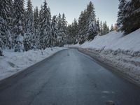 there is a long empty road surrounded by trees in the winter with snow on it