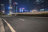 an empty road that has some very tall buildings in the background and a green fence