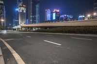 an empty road that has some very tall buildings in the background and a green fence