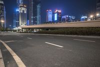 an empty road that has some very tall buildings in the background and a green fence