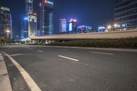 an empty road that has some very tall buildings in the background and a green fence