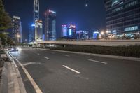 an empty road that has some very tall buildings in the background and a green fence