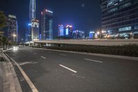an empty road that has some very tall buildings in the background and a green fence