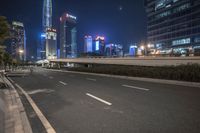 an empty road that has some very tall buildings in the background and a green fence