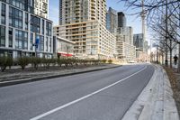 the paved road in front of tall buildings is empty of people and traffic signs from nearby