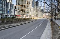 the paved road in front of tall buildings is empty of people and traffic signs from nearby