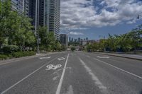 the empty road with no vehicles on it is surrounded by tall buildings and trees in the distance