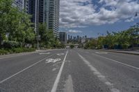 the empty road with no vehicles on it is surrounded by tall buildings and trees in the distance