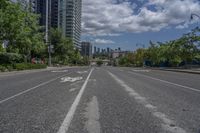 the empty road with no vehicles on it is surrounded by tall buildings and trees in the distance