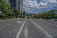 the empty road with no vehicles on it is surrounded by tall buildings and trees in the distance