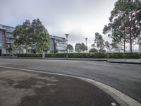 an empty street in front of two tall buildings near some trees and bushes on either side