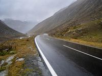 an empty road surrounded by tall, rocky mountains on a cloudy day in scotland stock photo