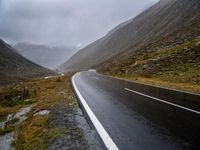 an empty road surrounded by tall, rocky mountains on a cloudy day in scotland stock photo