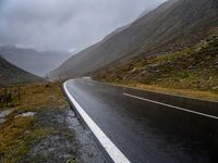 an empty road surrounded by tall, rocky mountains on a cloudy day in scotland stock photo