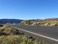 an empty road in a valley surrounded by green vegetation and mountains with a blue sky