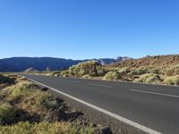 an empty road in a valley surrounded by green vegetation and mountains with a blue sky