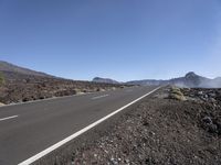 a road near the mountain side in the foggy sun day, and on the opposite bank are hills