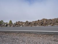 an empty road surrounded by rocks and shrubs on a bright cloudy day with clouds in the blue sky