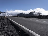 a view of a lone empty road with mountain range in the background and low cloud