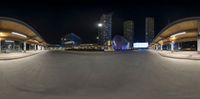 a empty road is seen at night with tall buildings in the distance and street lights in the foreground