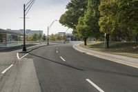 a empty road with street lamps along the side of it that are green trees and some building on both sides