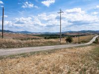 the road is empty near the telephone poles and an open field of wheat and rolling hills