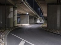 the empty road is under a very overpass that has an overhead lamp beside it